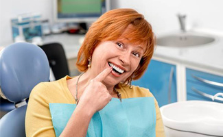 Smiling senior woman in dental chair pointing to teeth