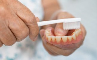A patient using a toothbrush to clean their denture