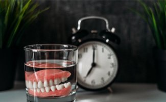 A pair of dentures set in a glass of denture solution
