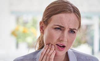 Woman holding her cheek due to dental emergency in Reno