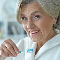 woman brushing teeth after getting dental implants in Reno