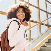 Teen girl with backpack smiling while walking upstairs