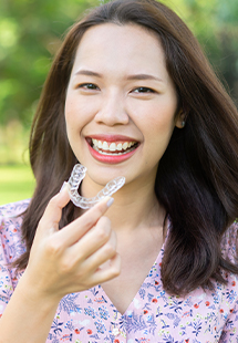 smiling woman holding clear dental aligner
