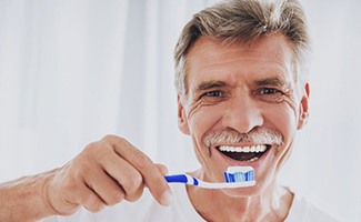 older man in white t-shirt brushing his teeth 