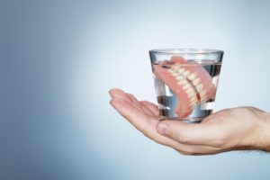 hand holding a glass of water with dentures in Reno 