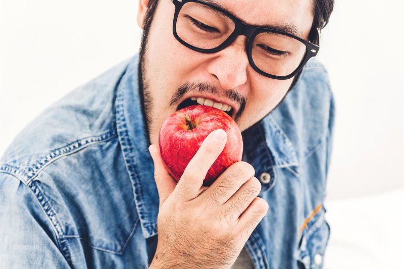 man with dental implants biting into hard apple in Reno
