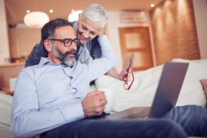 a man sitting on a couch with a laptop with his wife hugging him 