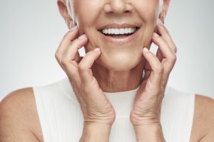 close up of woman in a white sweater vest smiling and touching her jaw with her fingers