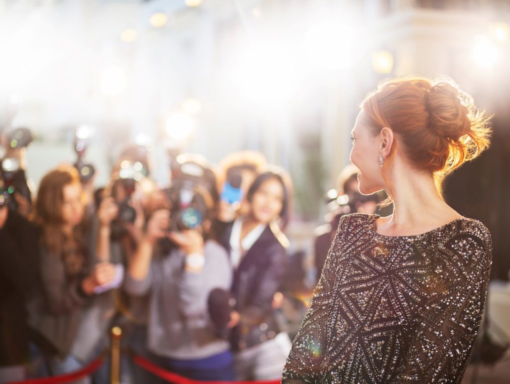 Woman with red hair smiling at paparazzi on red carpet