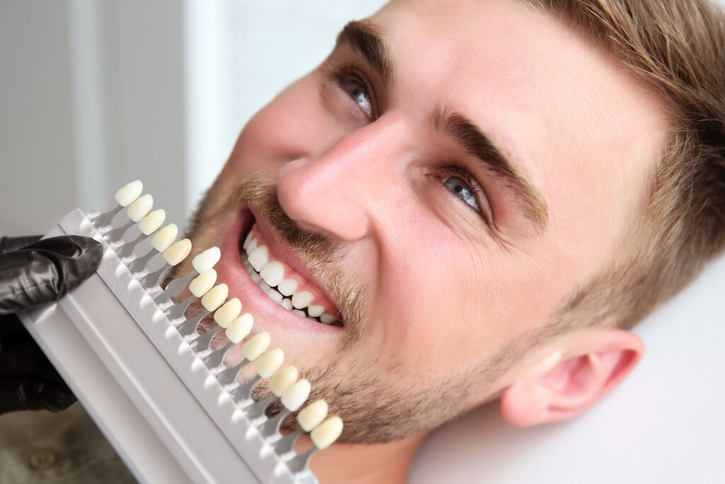 Dentist holding shade guide to man's teeth