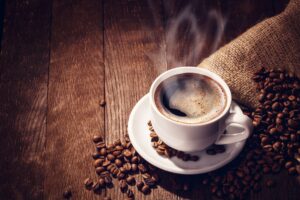 Cup of coffee on white saucer on wooden surface with spilled beans